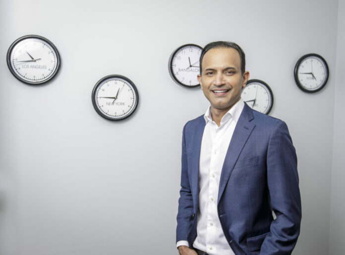 Near CEO and founder Anil Mathews poses with clocks representing where his company has offices at his office in Pasadena, CA. May 25, 2022. Photo by David Sprague