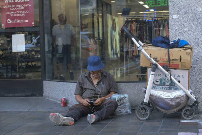 A homeless person sits on the sidewalk outside a Burlington store on Broadway and 7th street in downtown Los Angeles. (Photo by Ringo Chiu)