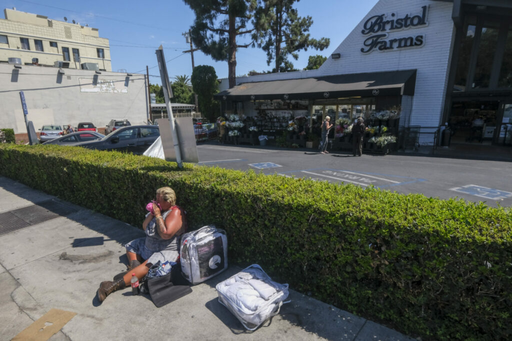 A homeless woman sits on the sidewalk in front of Bristol Farms near Fairfax Ave. and Sunset Blvd. in Los Angeles, Aug. 16, 2022. (Photo by Ringo Chiu)