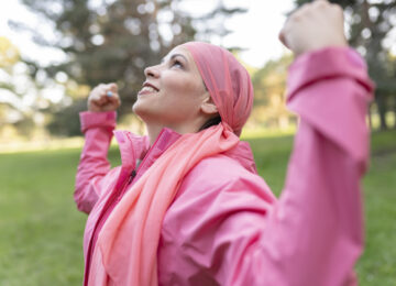 Medical and health concept. Healthy woman showing her power fist against female cancer She is wearing a pink scarf and a pink sweater. fight against cancer.