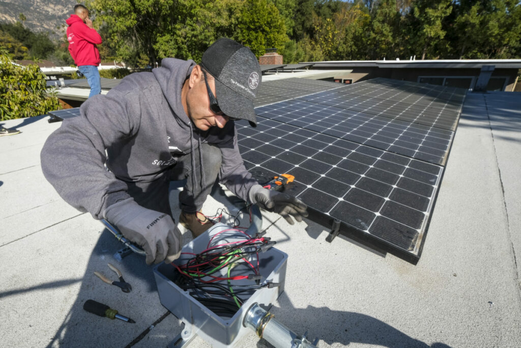 A worker installs the solar panel system on the rooftop of a home in Altadena. (Photo by Ringo Chiu)
