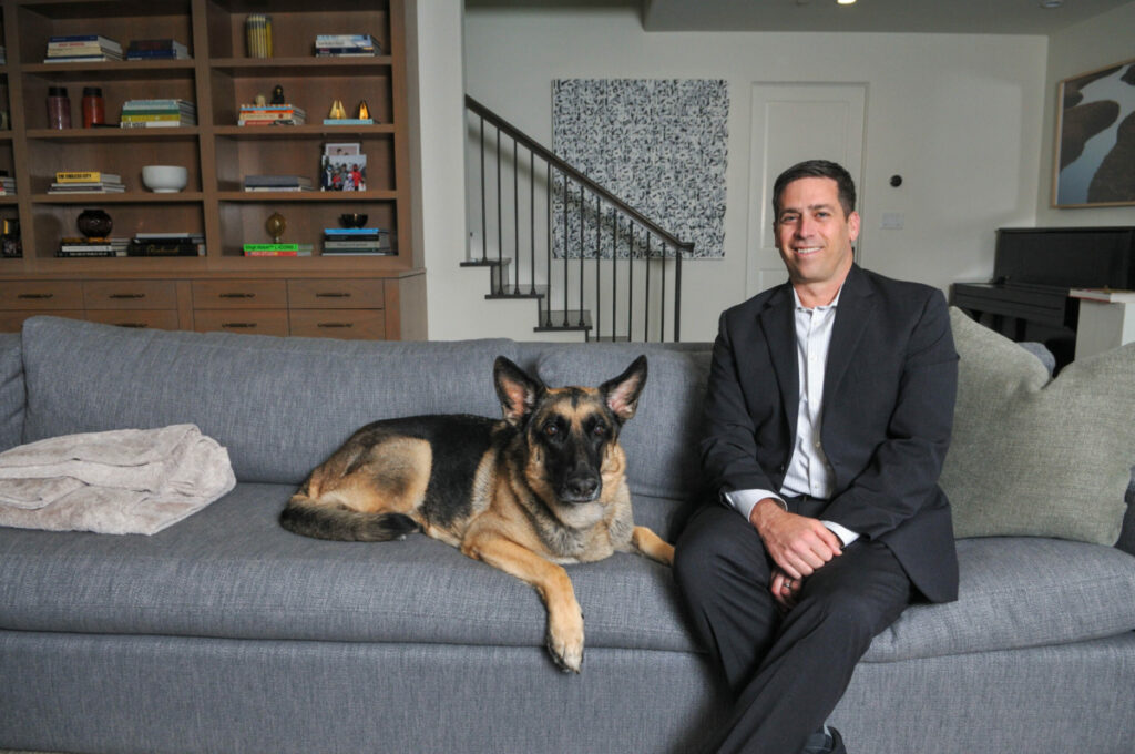 Howard Kozloff, Founder & CEO, Noblespace sitting on the couch at his home office with his dog, Atlas.